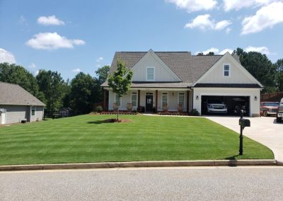A house's garage surrounded by a green lawn next to the road.