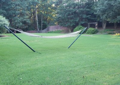 A mesh hammock in the middle of a green lawn and surrounded by trees.