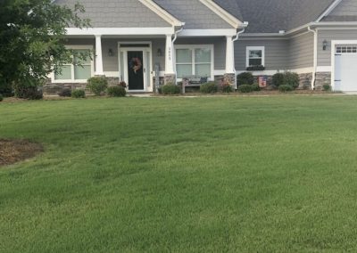 A traditional gray and white house preceded by a large green garden.