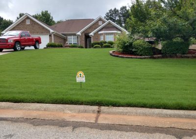 An All Turf sign in the middle of a yard next to a red truck.
