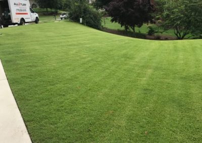A car in the back of a large green field.