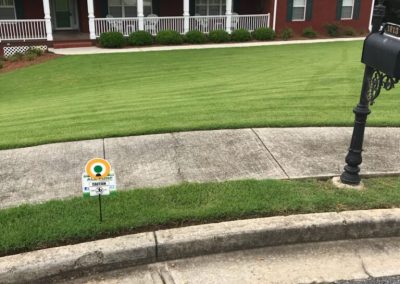An All Turf sign near a mailbox in front of the yard of a red house.