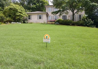 An All Turf sign in the middle of a yard in front of a traditional house.