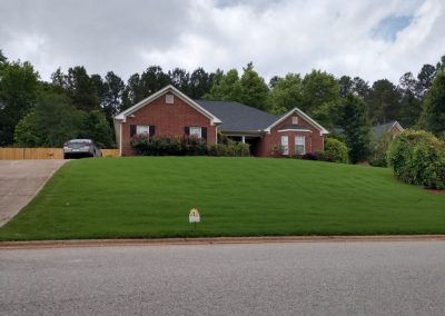 A red brick house surrounded by trees and with a nice garden next to the street.