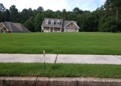 A white wooden house surrounded by trees and with a nice garden next to a sidewalk.