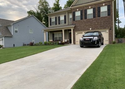 A parking zone in front of a traditional house with a green front yard.