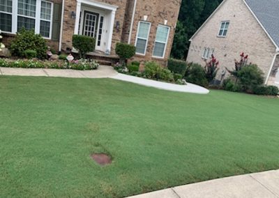 A patio surrounded by flower beds in front of a brick house.